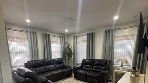 Un salon moderne avec deux canapés en cuir noir, un tapis à motifs, un plancher en bois et un téléviseur posé sur un meuble.