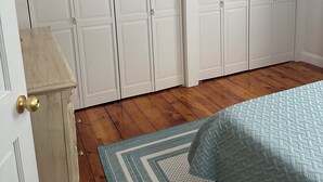 Une chambre avec un plancher en bois, un lit recouvert d’une courtepointe et une armoire à deux portes.