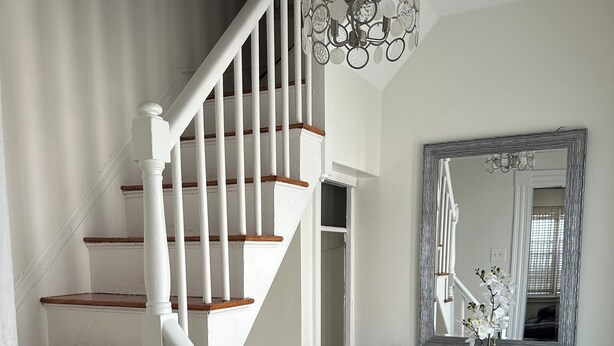 Un escalier avec des rampes blanches et des marches en bois, menant à un palier où se trouvent une console de couleur turquoise et un miroir.
