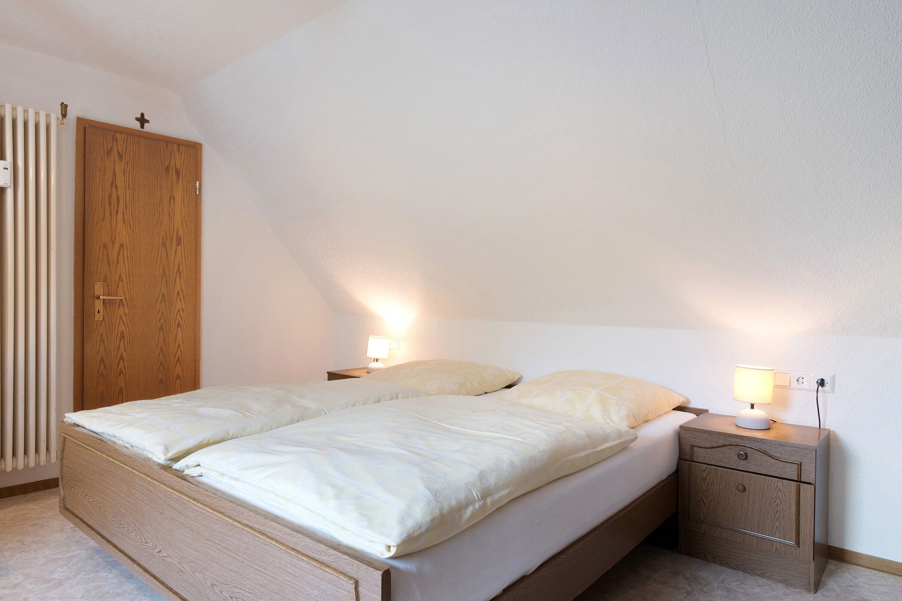 A bedroom with a wooden bed, two bedside tables with lamps, a wooden wardrobe, and a radiator.