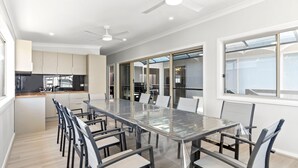 A modern kitchen with a dining area, large windows, and a ceiling fan. - Suitable for Large Groups / Near Beach / Family Fr (The Entrance North)