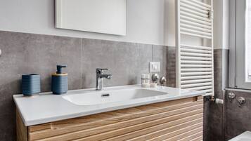 Un bagno moderno con un lavandino bianco, un mobile contenitore in legno, piastrelle grigie e un portasciugamani bianco.