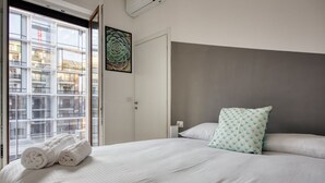 Hotellihuone, jossa on suuri sänky, ikkunasta avautuva näkymä rakennuksiin ja ovi, jossa on taulu.