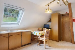 Une cuisine avec une fenêtre, des meubles de rangement en bois, une table à manger avec des chaises et un téléviseur.