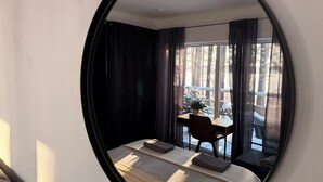 A bedroom with a large bed, a desk, and a chair. There is a window with curtains, and a view of trees outside.