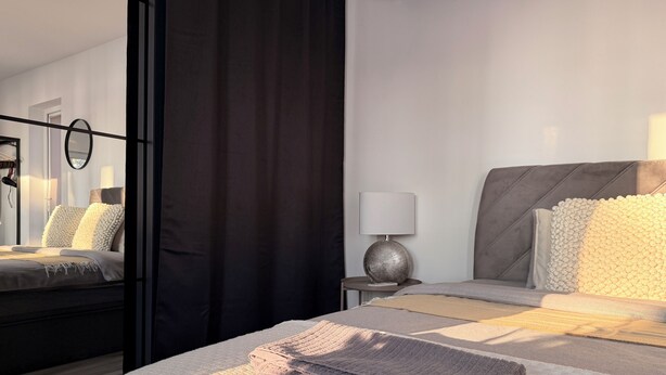 A modern bedroom with a bed, bedside tables, and a mirror.