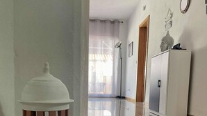 A hallway with a tiled floor, a white pillar with a textured base, a door, and a cabinet with a decorative item on top.
