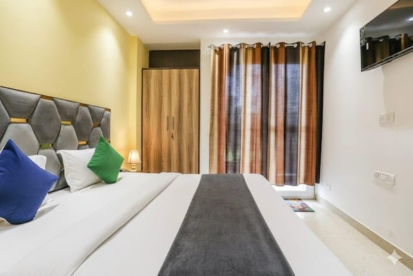 Habitación de hotel con cama, cabecera, armario, televisor y ventana con cortinas.