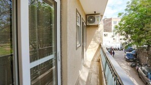 A balcony with large windows, a ceiling fan, and a view of a street with parked cars and buildings. - hotel aiims 20 four 7 (New Delhi)