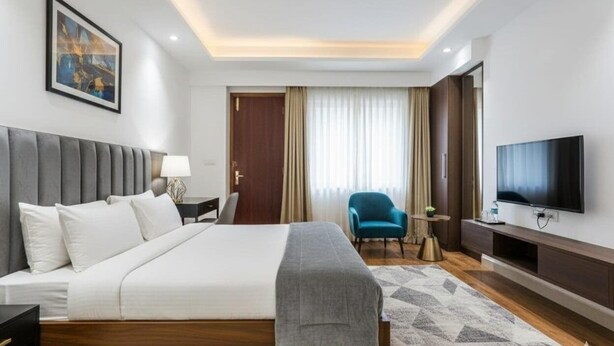 A modern hotel room with a large bed, a TV, a desk, and a chair. - hotel aiims 20 four 7 (New Delhi)