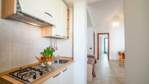 Cucina con piano cottura a gas, mobili bianchi e lavello. In secondo piano si vede un'area pranzo con tavolo e sedie.