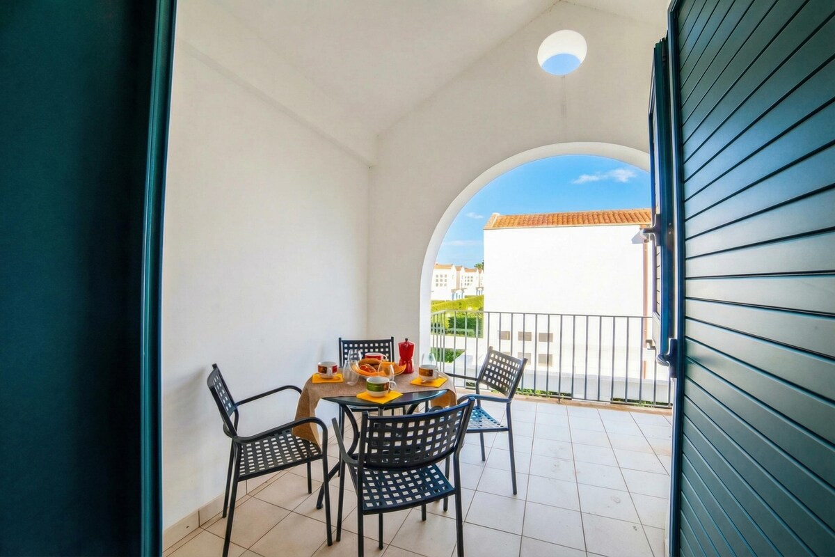 A balcony with a table set for two, chairs, and a view of buildings in the background.