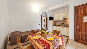 Una sala da pranzo con un tavolo apparecchiato per quattro persone, un divano e una cucina sullo sfondo.