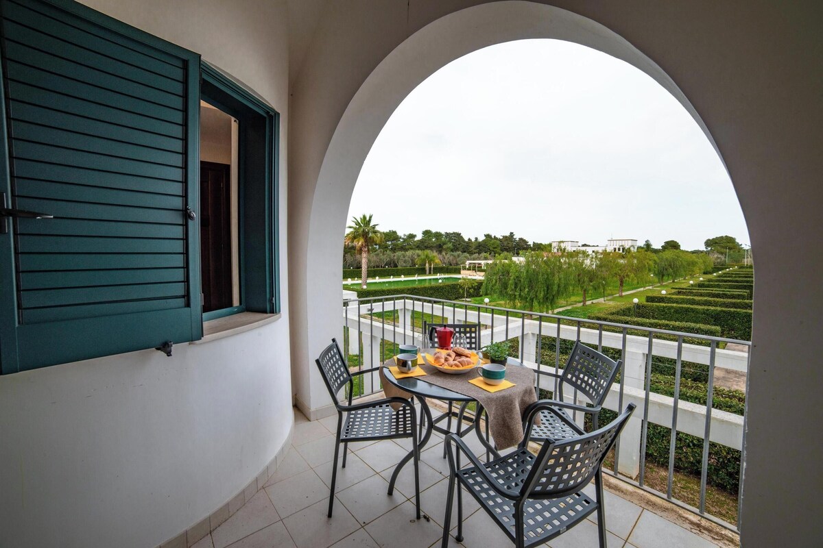 A balcony with a table, chairs, and a view of a landscaped garden.