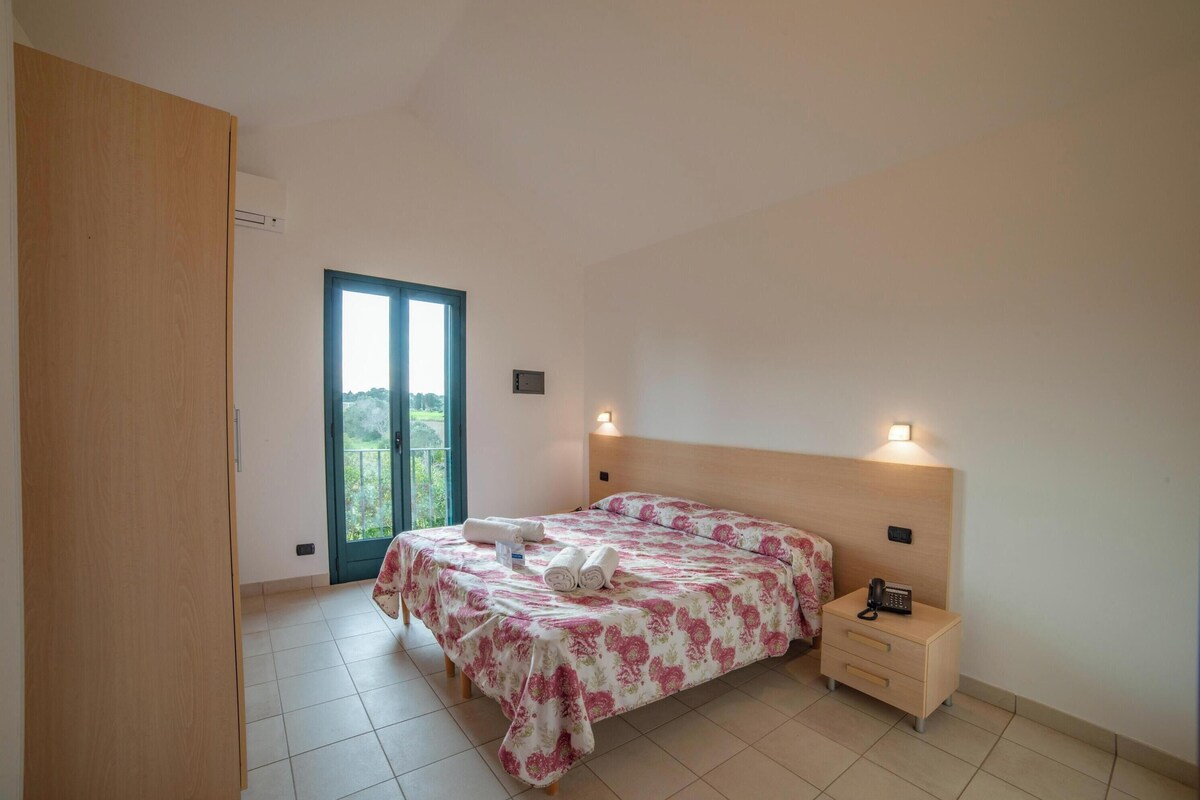 A bedroom with a bed, bedside table, and a view through a door.