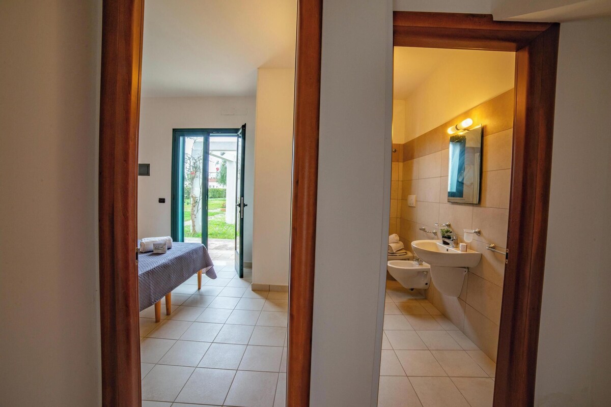 A hotel room with a bed, a bathroom with a sink and toilet, and a view of the outside.