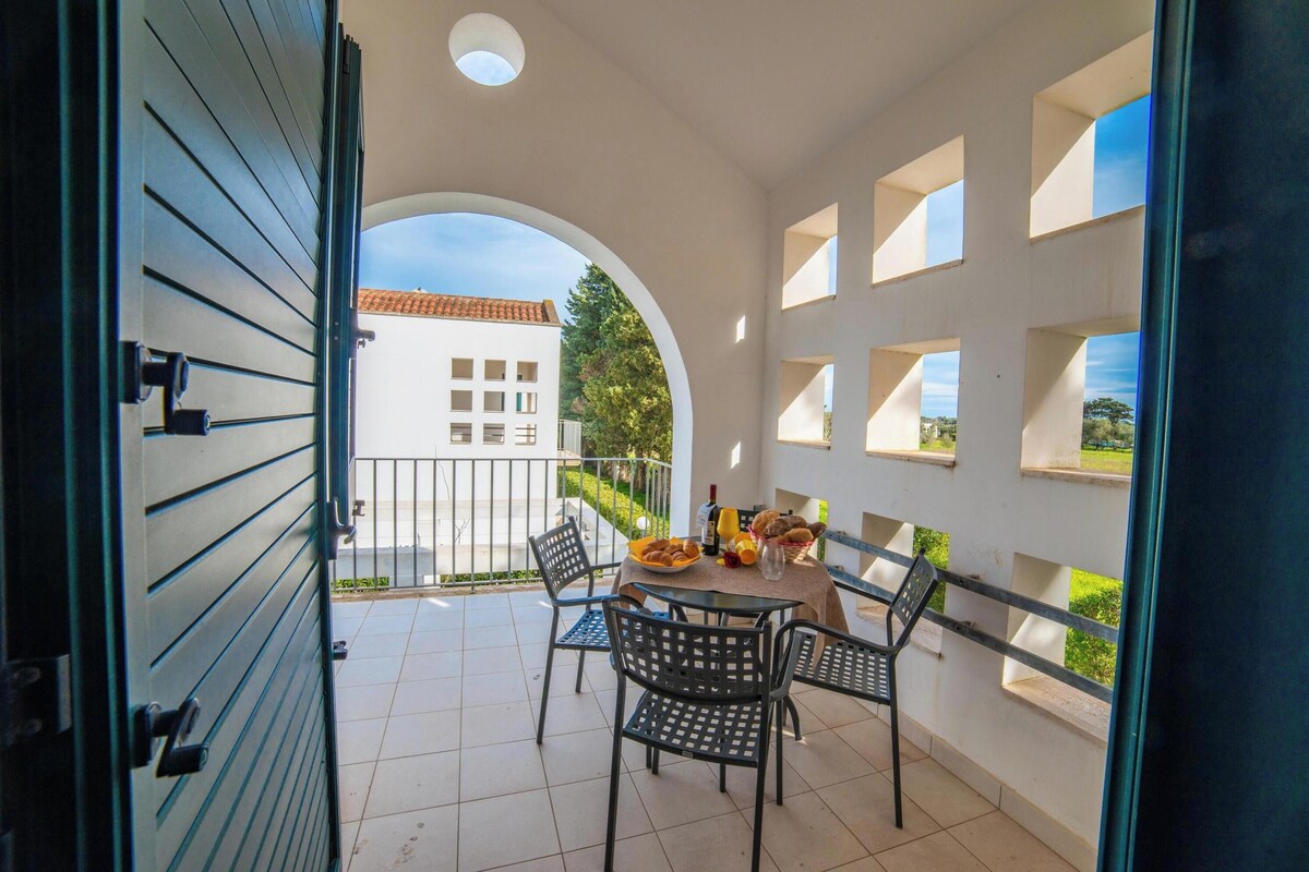 An open balcony with a table set for dining, chairs, and a view of a building with a tiled roof.