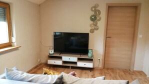 Een woonkamer met een flatscreen televisie op een houten standaard, een bank en een deur.