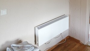 Een kamer met een wandtelevisie, een witte radiator en een houten vloer.