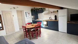 A compact living space with a sofa, a dining table with chairs, a kitchen area with cabinets, and a refrigerator.