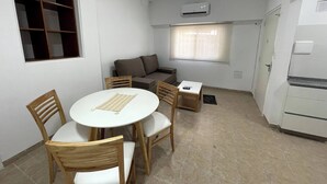 A compact living space with a dining area, a sofa, a window with blinds, and a built-in air conditioning unit. - Comfortable Retreat Near River Plate's Monumental Stadium (Buenos Aires)