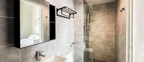 A modern bathroom with a large mirror, a sink, a toilet, and a glass shower enclosure.