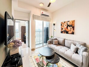 A modern living room with a sofa, a coffee table, a flat-screen TV, and a large window. - Glomac 121 Residences by Airhost (Petaling Jaya)