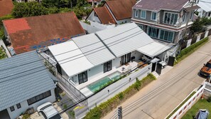 Une maison moderne à deux étages, dotée d’une piscine, de grandes fenêtres et d’un toit plat.