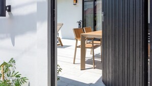 A modern outdoor patio with a wooden table and chairs, a white wall, and a black fence. - Newly Renovated Pool Villa with BBQ V296 (Koh Samui)