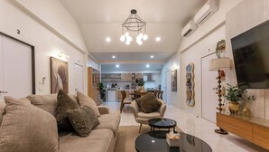 A modern living room with a sofa, coffee table, and TV. There is a kitchen in the background. - Newly Renovated Pool Villa with BBQ V296 (Koh Samui)