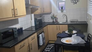 A compact kitchen with wooden cabinets, a black countertop, a built-in oven, and a sink. There's a decorative wall piece and a small potted plant on the counter. - Glams 2beds luxury stylish apartment (West Midlands)