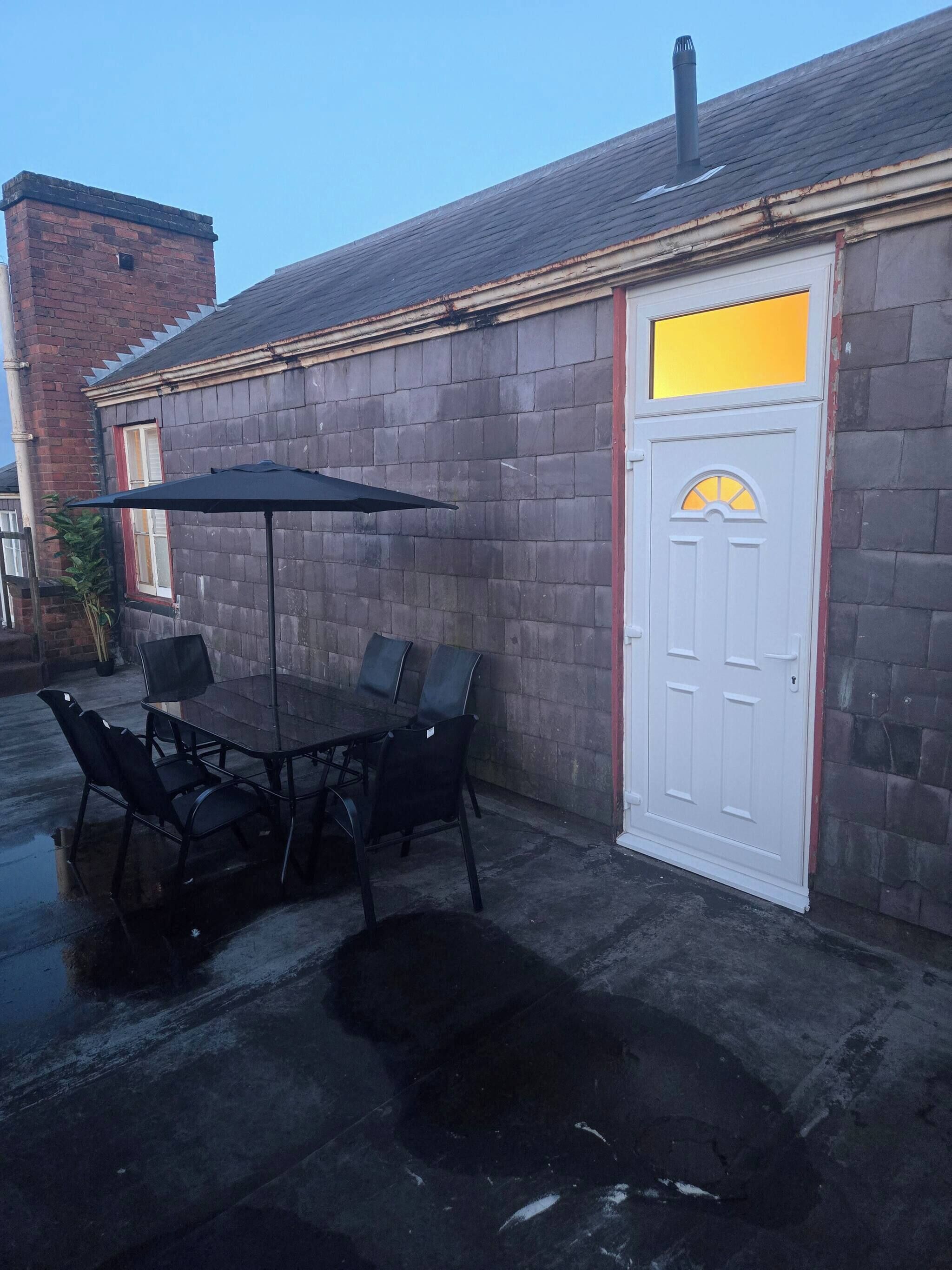 An outdoor patio with a table and chairs, a white door, and a brick wall.
