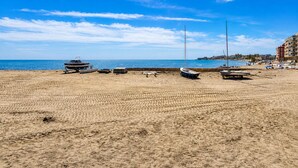 Ein Sandstrand mit mehreren Booten und einem Gebäude im Hintergrund.