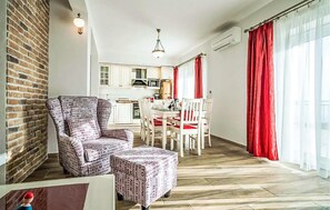A modern living room with a brick wall, a patterned armchair, a small table, and a dining area with a white table and red chairs. - Amazing home in Makarska with sauna (Makarska)