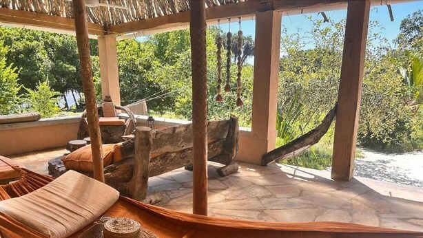 Eine Hängematte unter einer Holz-Pergola mit Steinboden, mit Blick auf eine üppige grüne Landschaft.