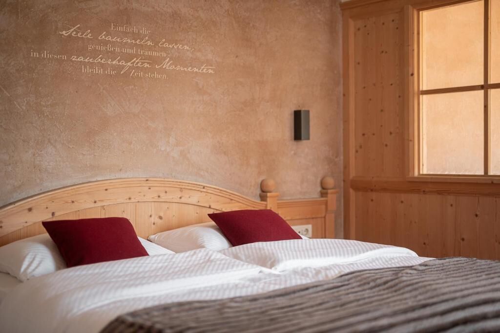 A bedroom with a wooden headboard, two red pillows, and a large window.