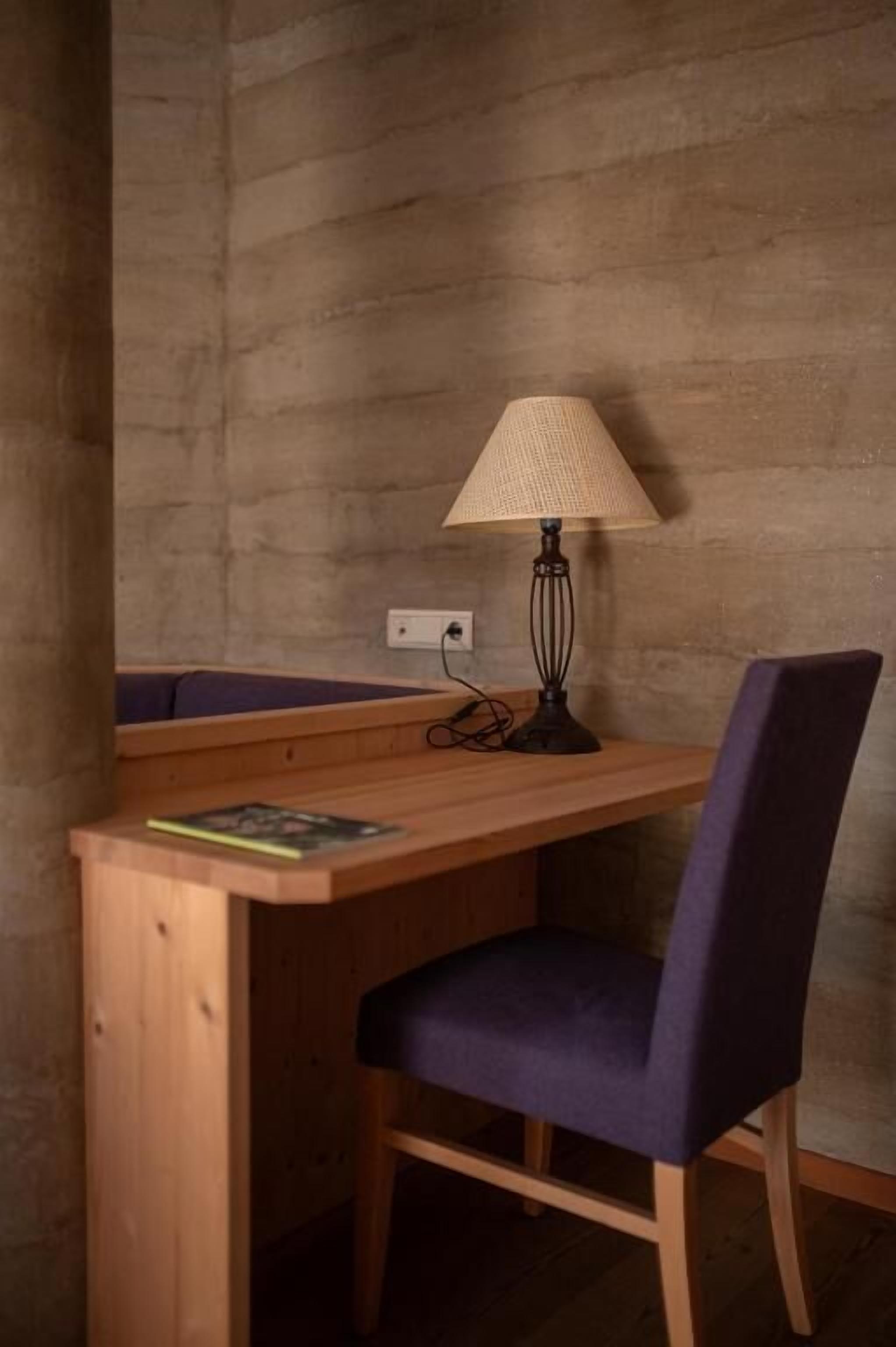 Ein Holztisch mit Lampe, Stuhl und Steckdose an einer strukturierten Wand.