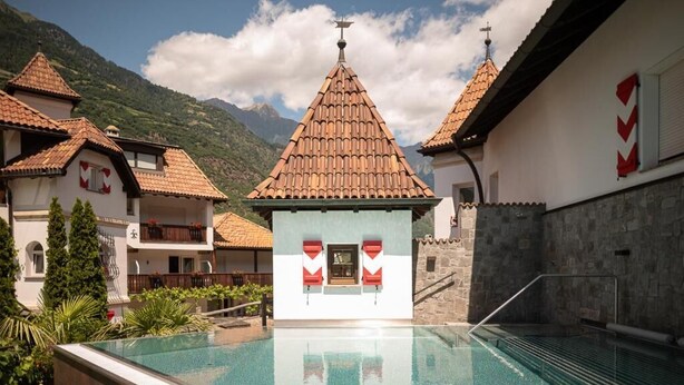 Una piscina con vistas despejadas a montañas, un edificio con tejado de baldosas y un muro de piedra.