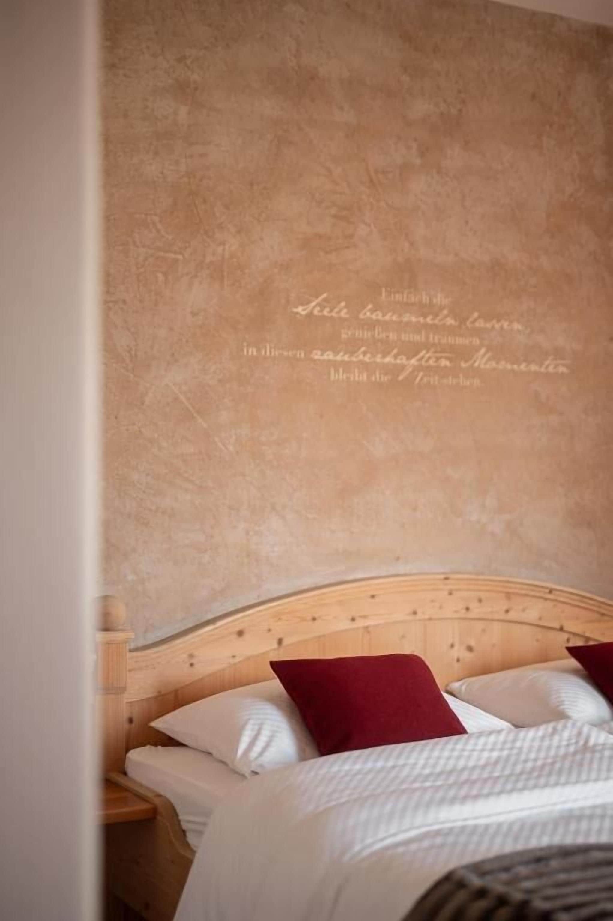 A bedroom with a wooden headboard, two beds with white and red bedding, and a textured wall with text.