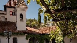 Un patio exterior con un edificio blanco que tiene una torre de campanas, rodeado de plantas en macetas y mobiliario de exterior.