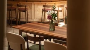 Una mesa de madera con cuatro sillas, un florero con flores y una cocina al fondo.
