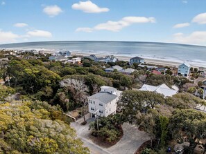 An aerial view of a coastal residential area with houses, dense greenery, and a beach in the background. - 1 Block to the  Beach + Game Room + Covered Deck | East Folly | Family Tides (Folly Beach)