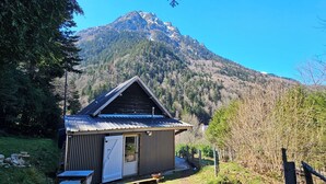 Una petita cabana de fusta amb teulada metàl·lica, envoltada d'arbres i una muntanya al fons.