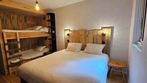 Una habitació amb una llitera, un llit individual i un petit tamboret de fusta.