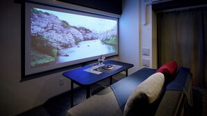 Une pièce dotée d’un écran de projection diffusant des images de paysages naturels, d’une table avec des verres et un vase, et d’un canapé agrémenté de coussins.