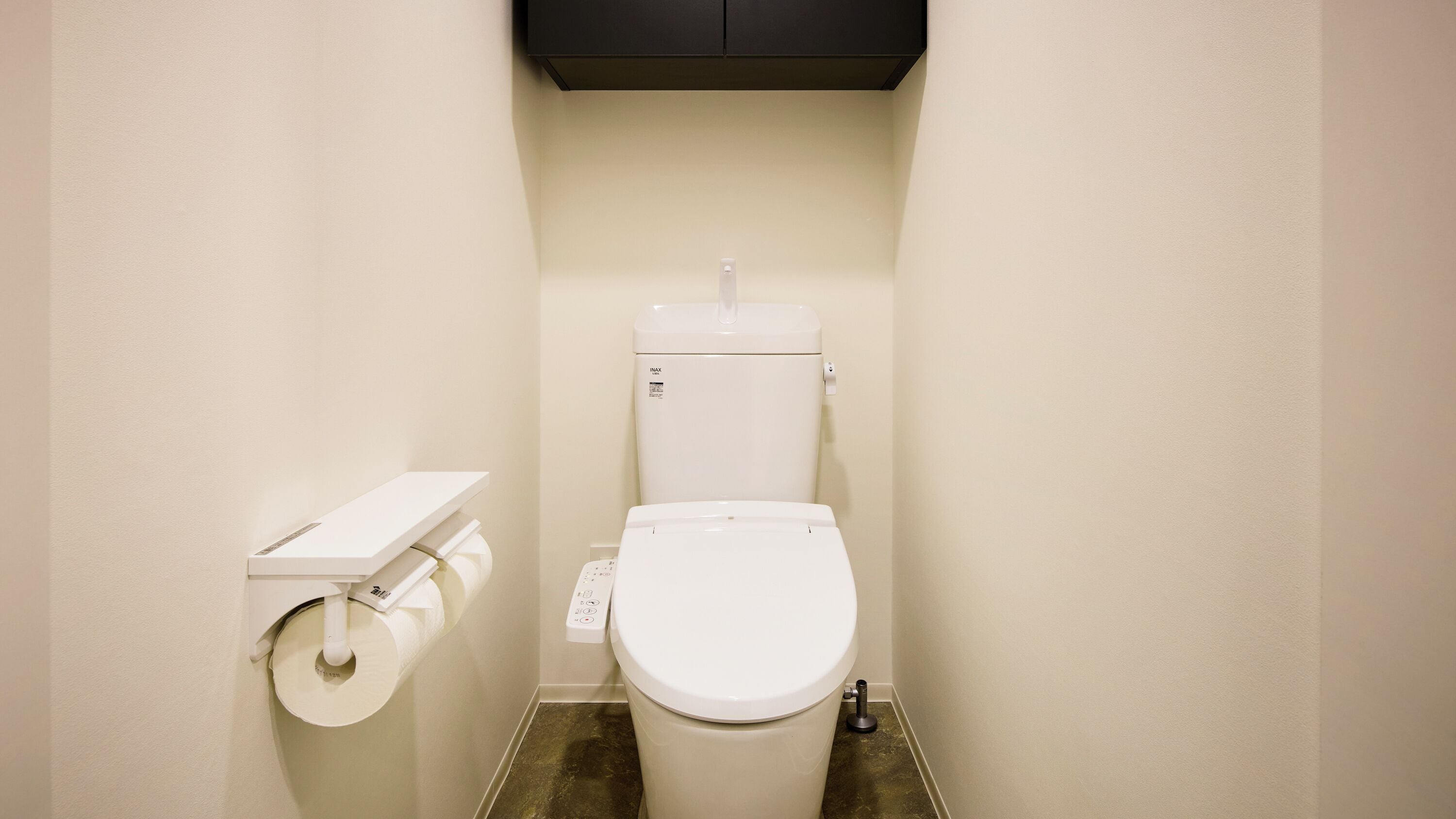 A small, clean bathroom with a toilet, a toilet paper holder, and a black cabinet above the toilet.