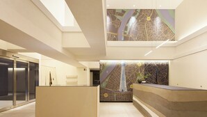 Un hall d’hôtel moderne avec un comptoir d’accueil, une fresque représentant une carte et un ascenseur en verre.
