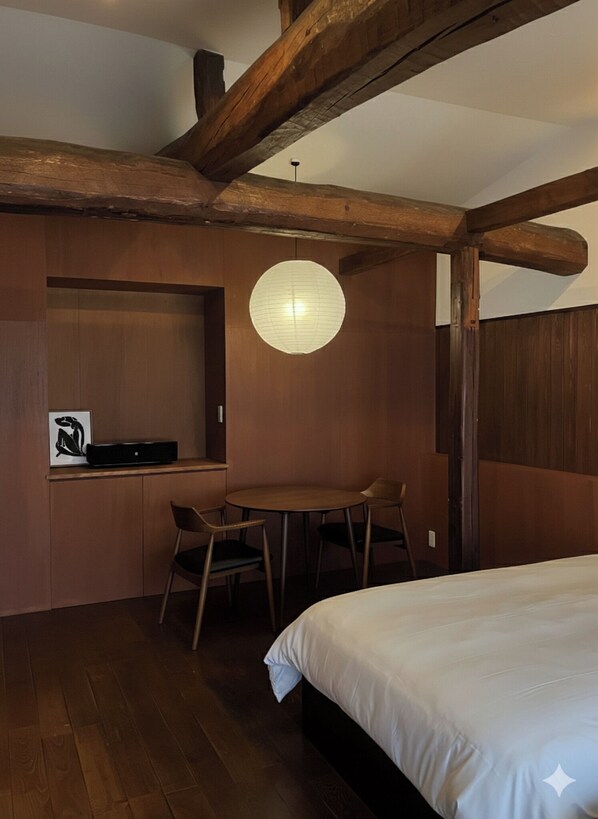 Ein Schlafzimmer mit Holzbalkendecke, einer runden Wandleuchte, einem Bett und einem kleinen Tisch mit Stühlen.