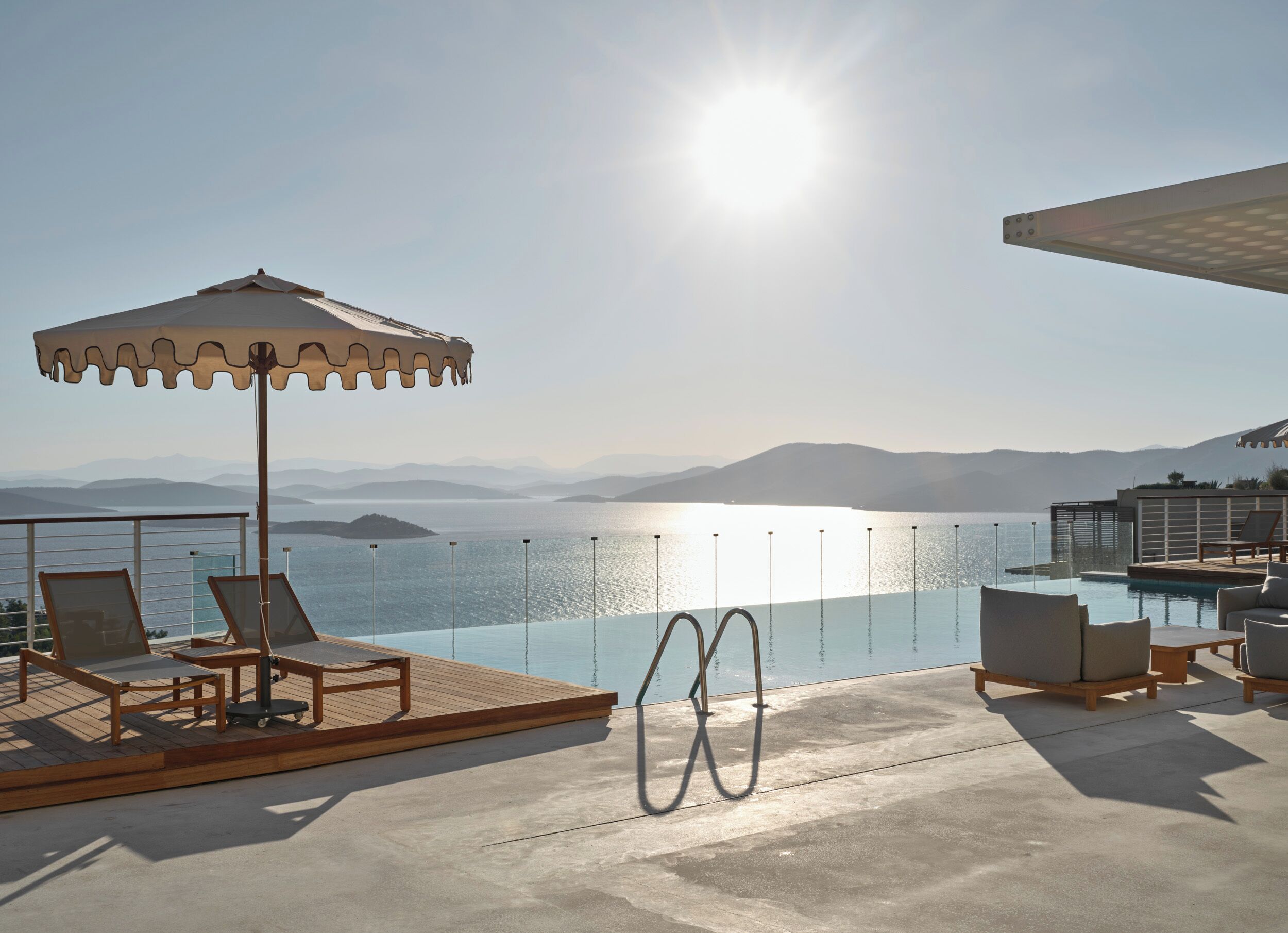 Zona junto a la piscina con sillones de descanso, una sombrilla y vistas al mar y a las montañas.
