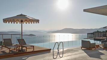 Zona junto a la piscina con sillones de descanso, una sombrilla y vistas al mar y a las montañas.